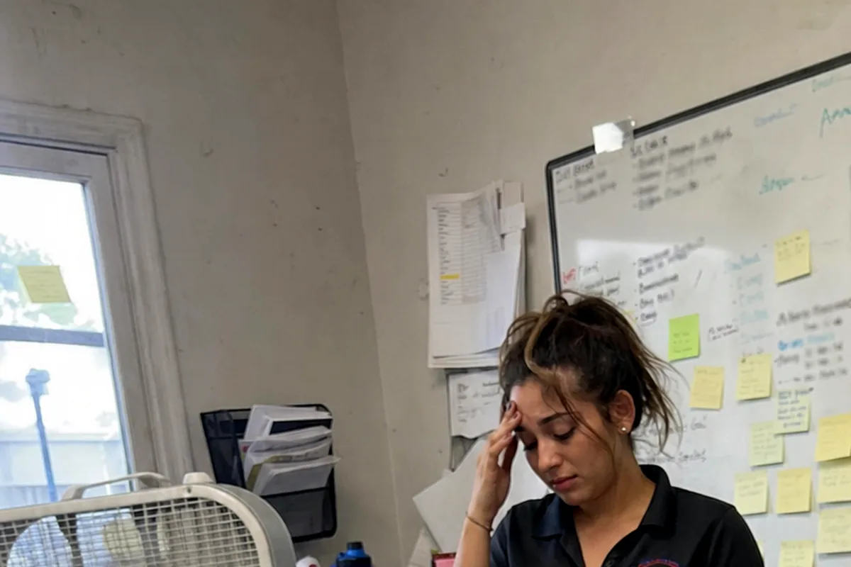 A cluttered small HVAC office desk with a phone, a job schedule whiteboard, and scattered paperwork.