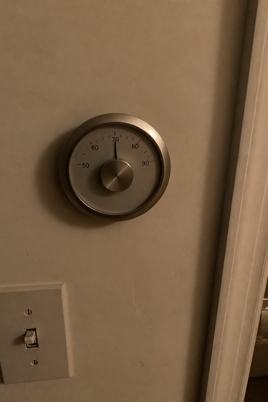 A brass thermostat dial glowing softly in the dark, its needle resting on 72 degrees.