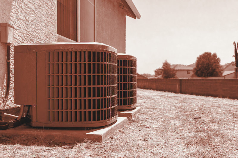 Residential AC condenser units baking in the sun beside a house during a summer heat wave.